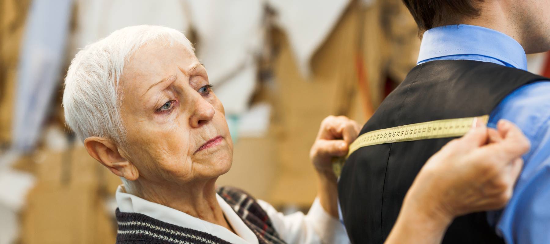 Older woman measuring back width of client waistcoat.