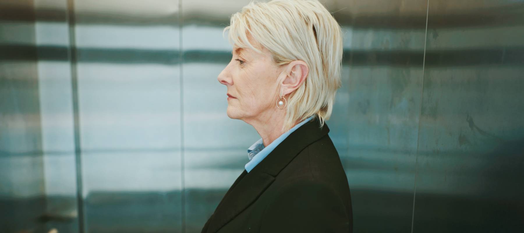 An older woman take an elevator down from her office.