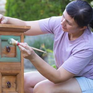 A woman prepares a piece of old furniture for resale.