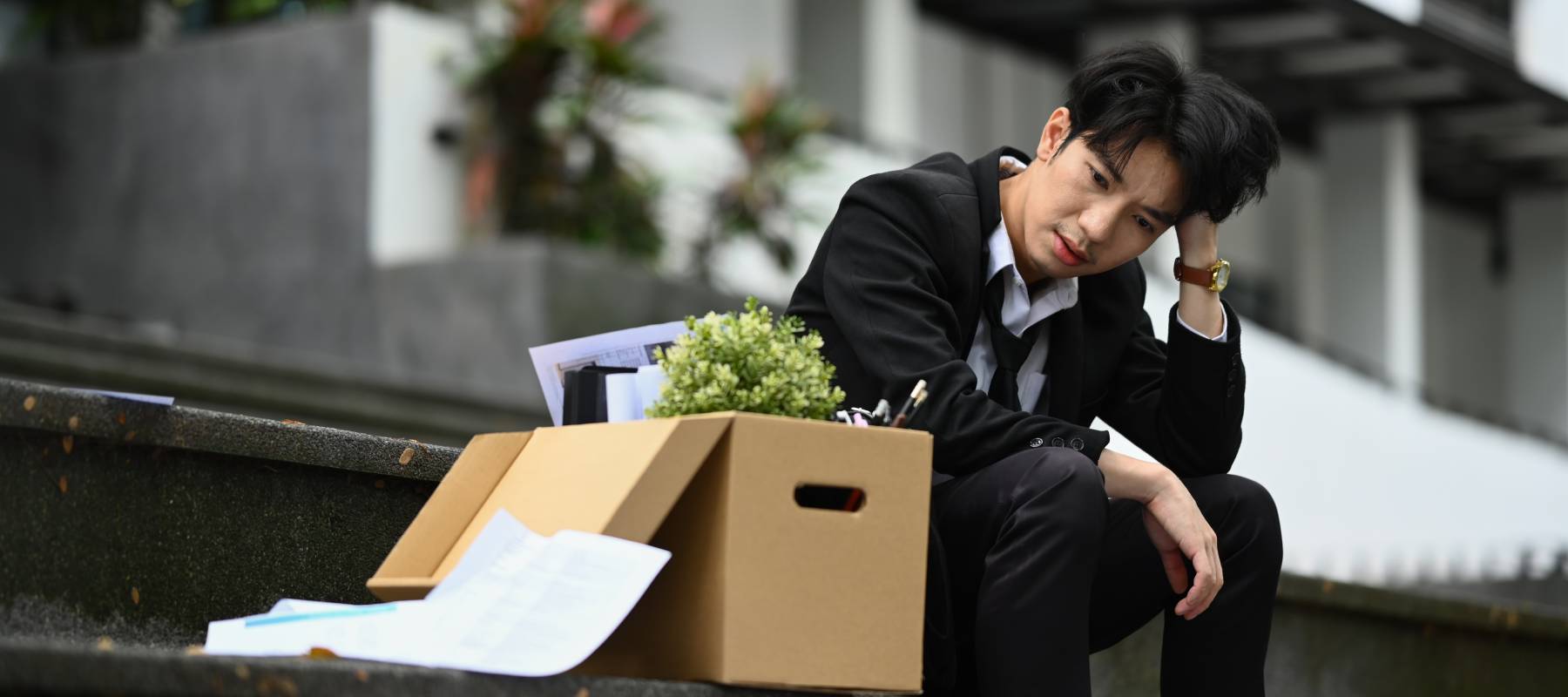 A distraught office worker sitting next to a box of his possessions.