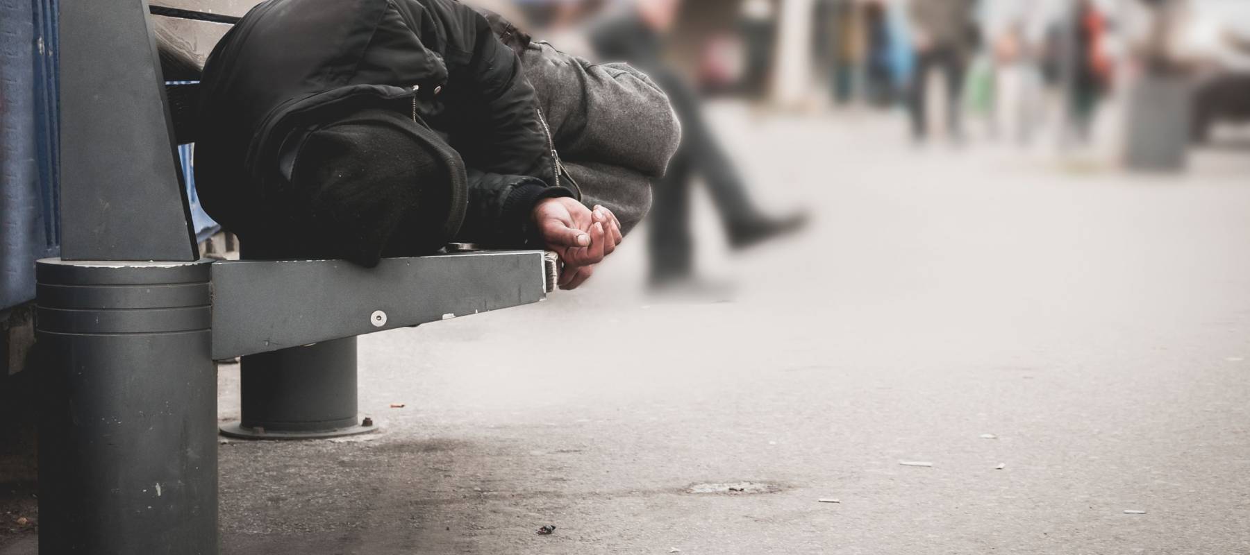 Homeless person lying down covered by a blanked in a pedestrian tunnel.