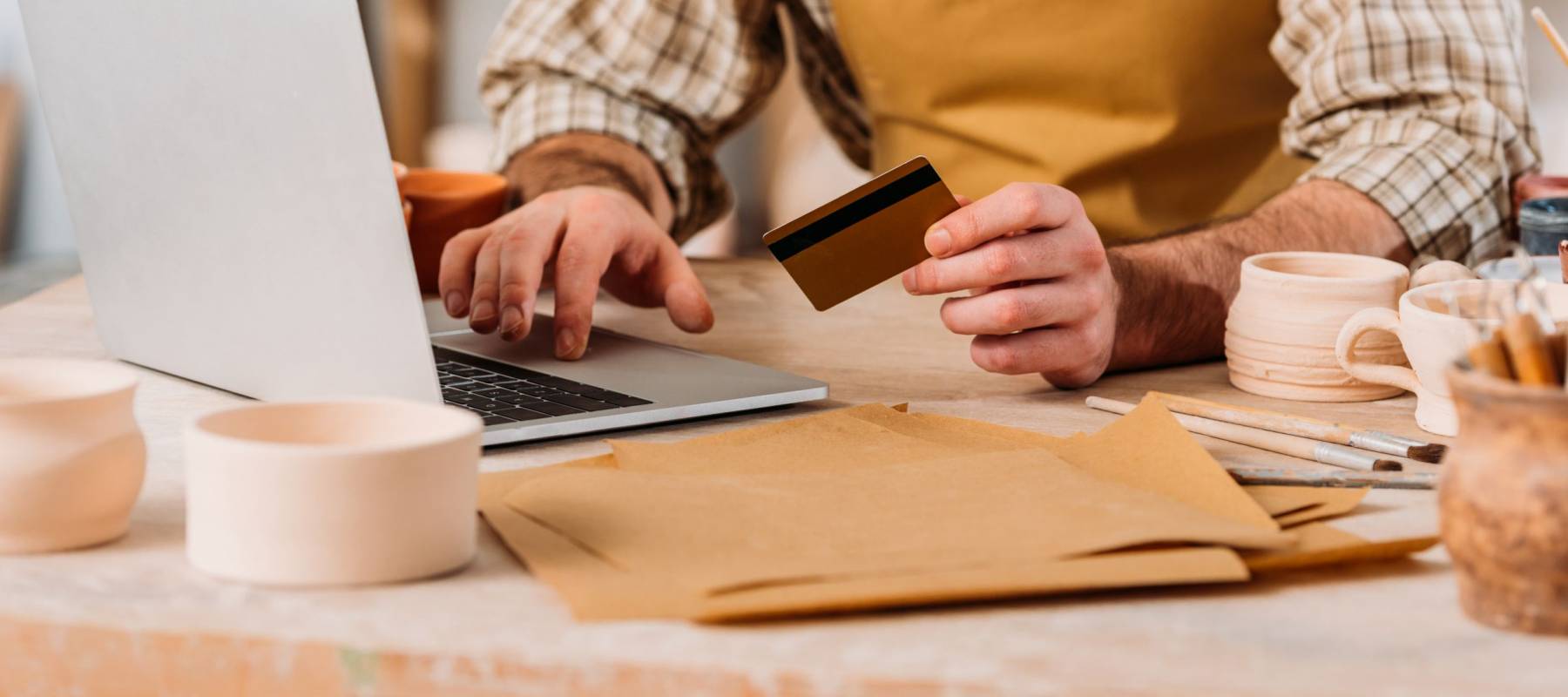 cropped view of potter shopping online with laptop and credit card in workshop