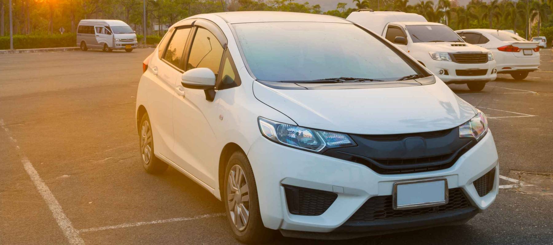 Cars parked in outdoor parking lot at a park in the evening time with  sunlight of sunset and beautiful orange sky background