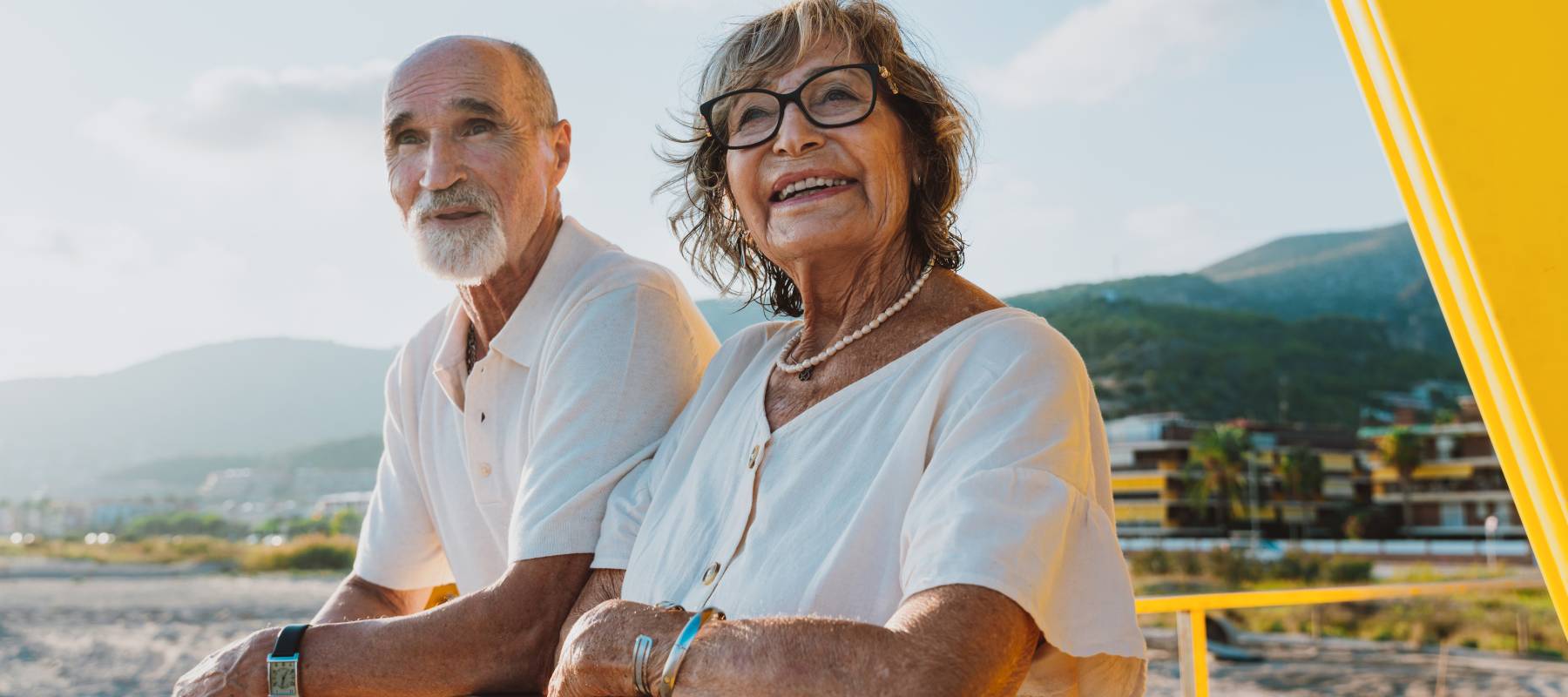 A retired couple, watching the ocean from a lifeguard tower, enjoying a break as they walk the beach.