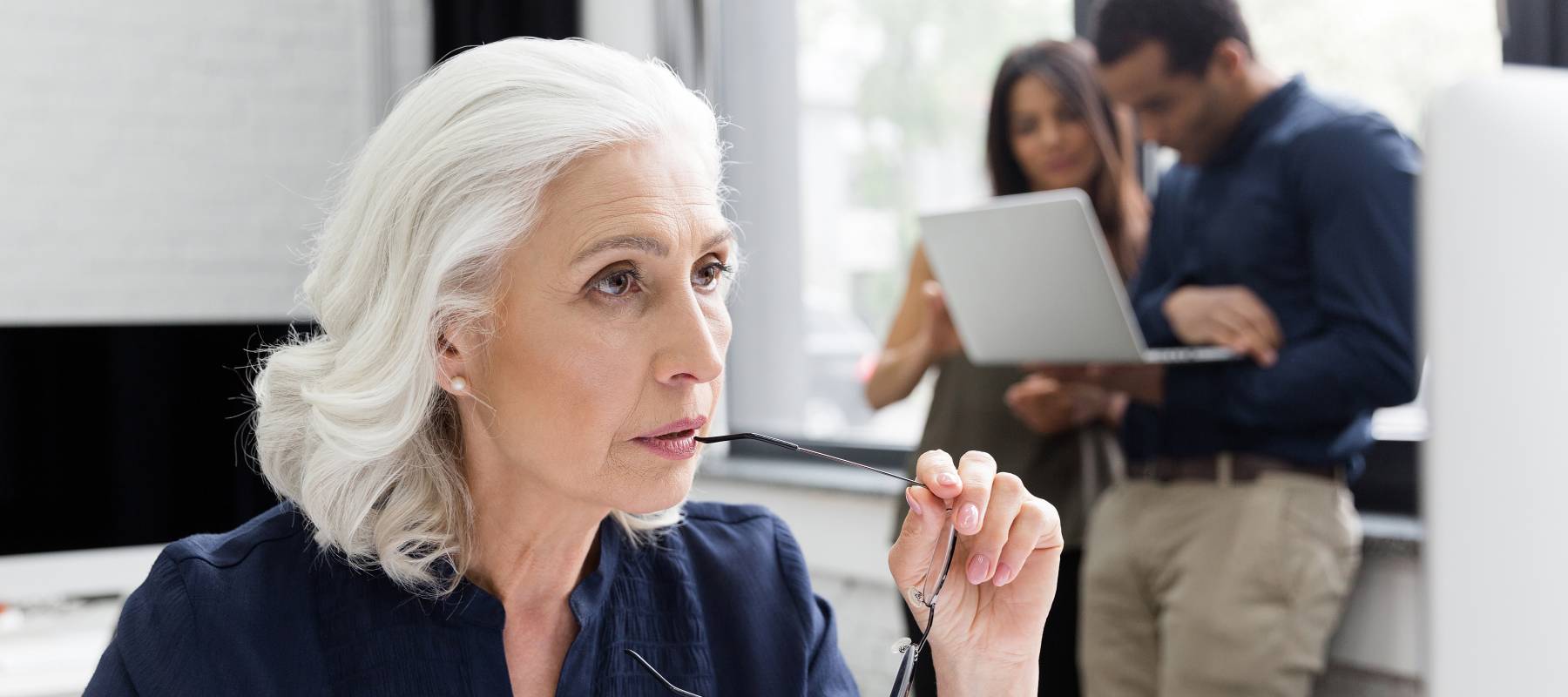 An older woman with brilliant white hair looks into the middle distance, deep in thought.