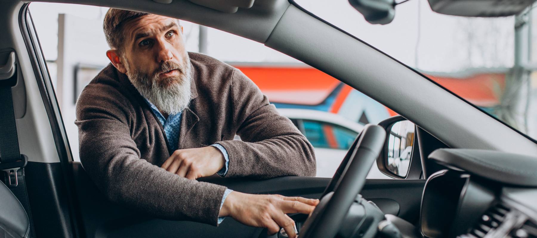 Older gentleman with gray hair and beard looking inside a new vehicle.