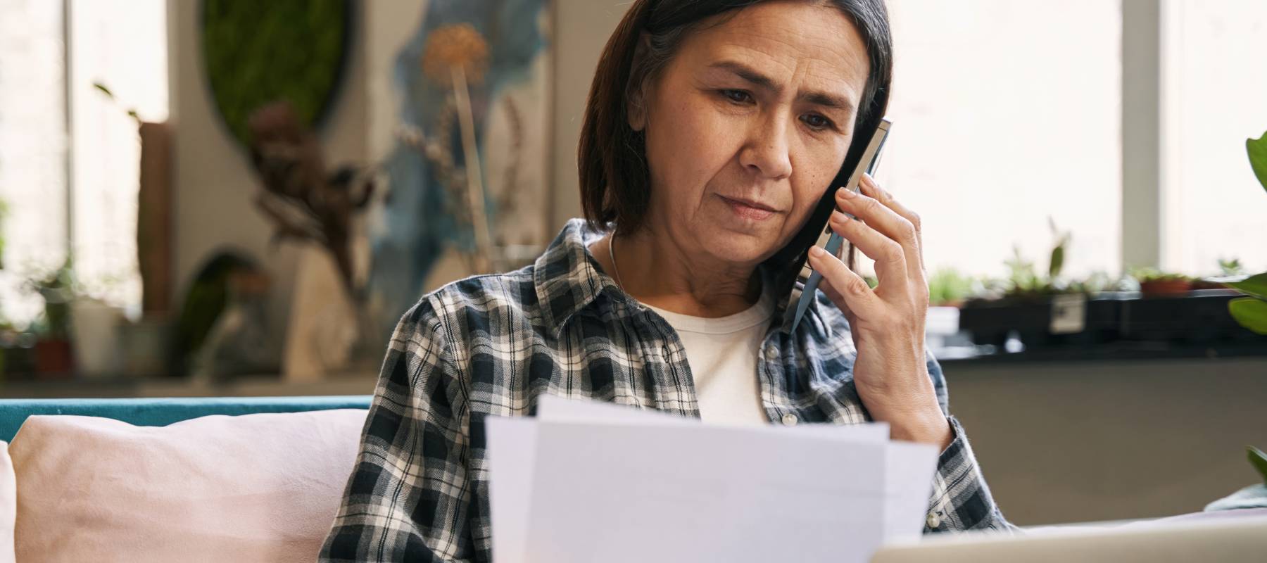 A woman, scrutinizing a billing statement, while on the phone.