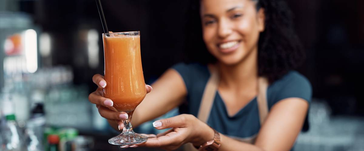 Close up of waitress holding glass of fresh fruit juice.