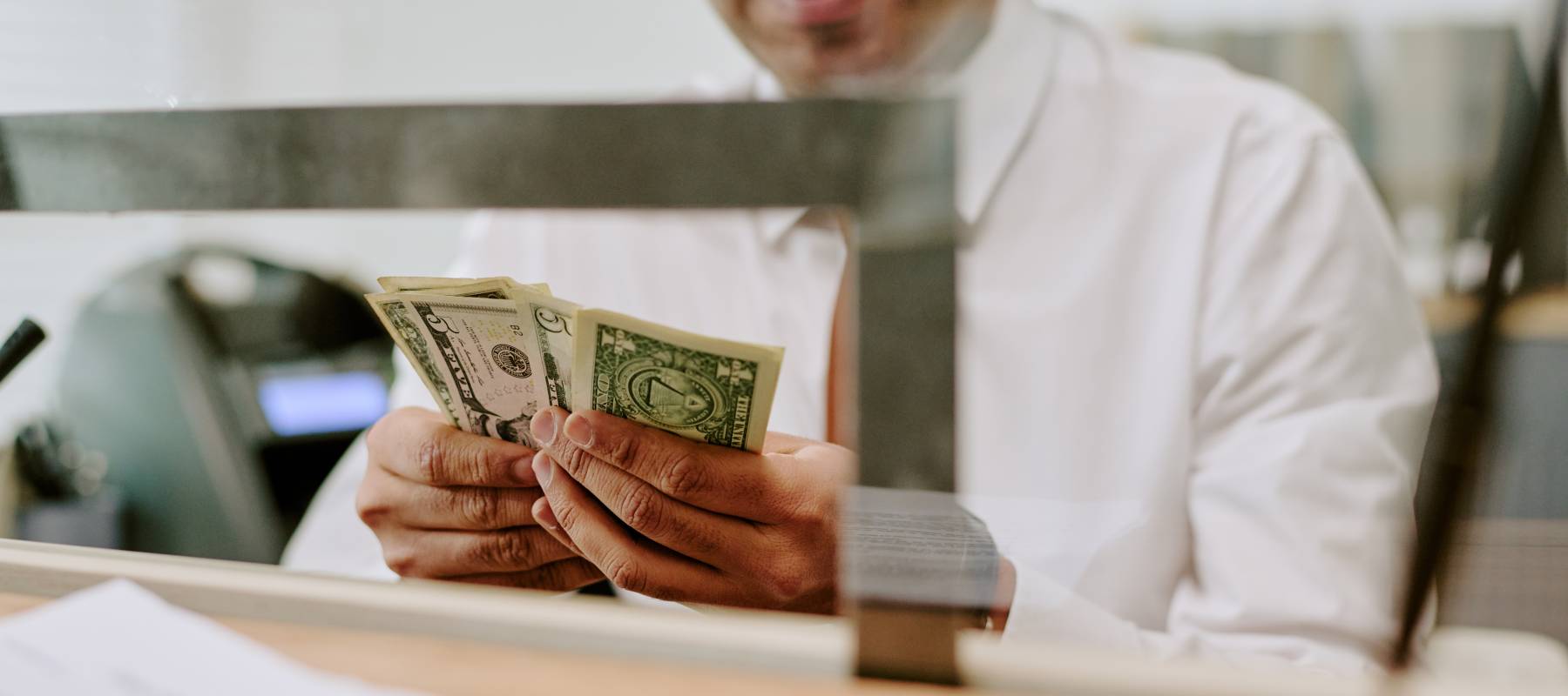 A bank teller counting money, with the value of the U.S. dollar losing 10% over the past year.