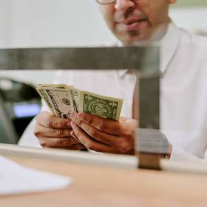 A bank teller counting money, with the value of the U.S. dollar losing 10% over the past year.