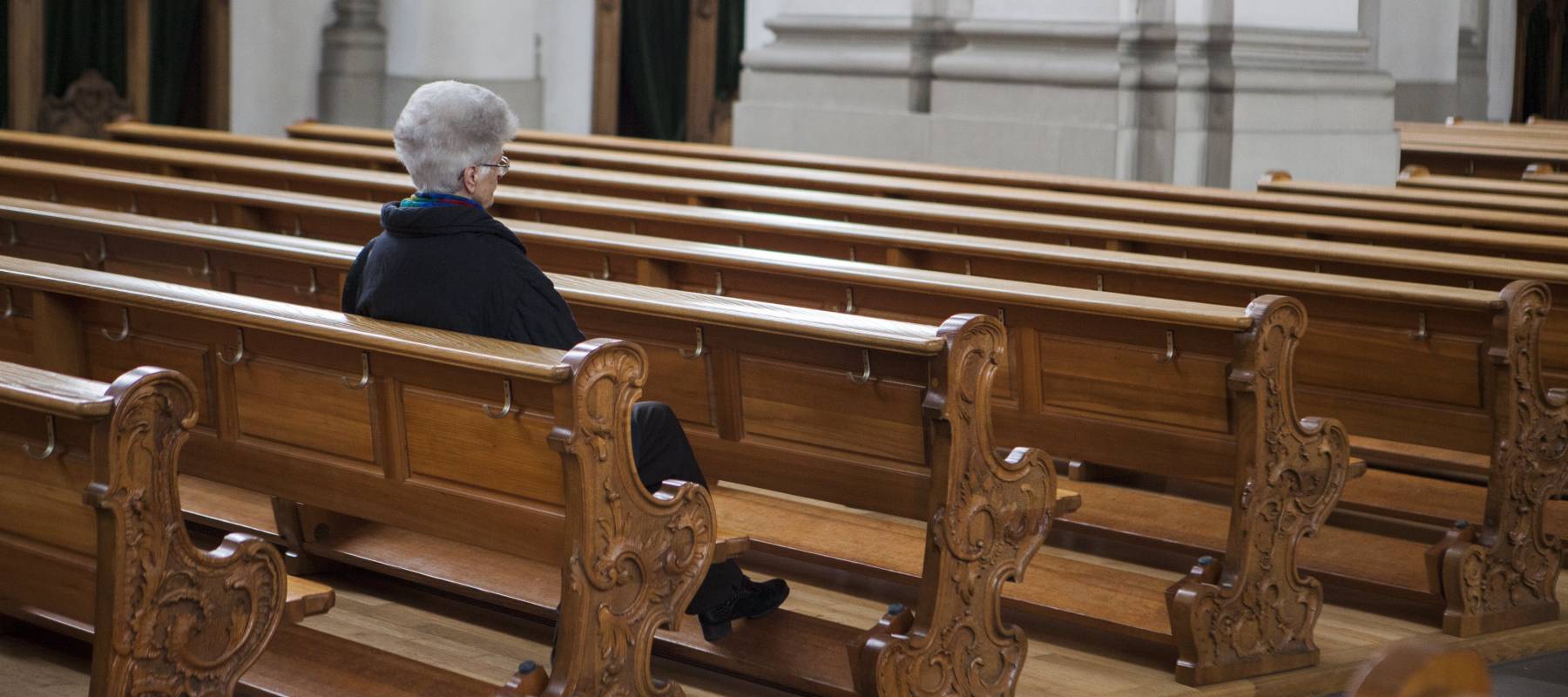 An older woman sits alone in a church pew.