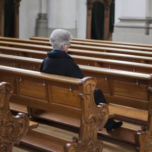 An older woman sits alone in a church pew.
