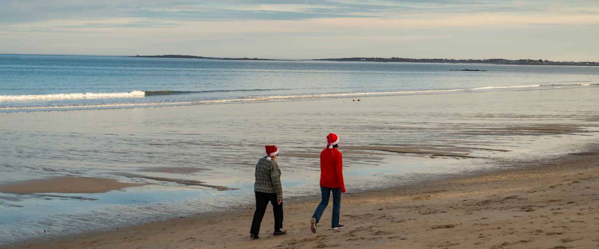 Rear view of a couple of women walking along the ocean shore in Maine USA. They wear father Christmas hat in December.
