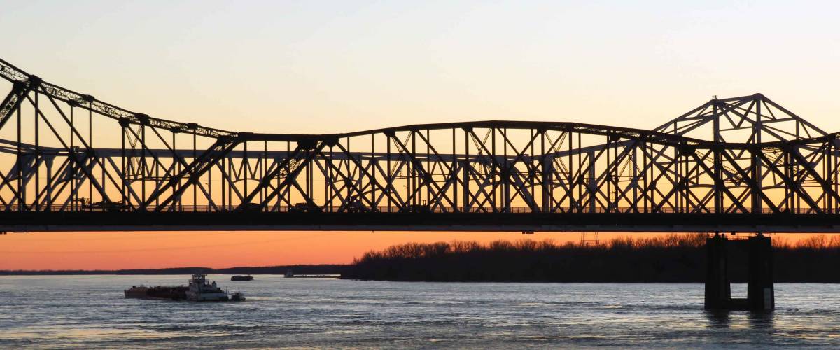 A steel bridge spans the Mississippi River at sunset in Vicksburg, Mississippi.