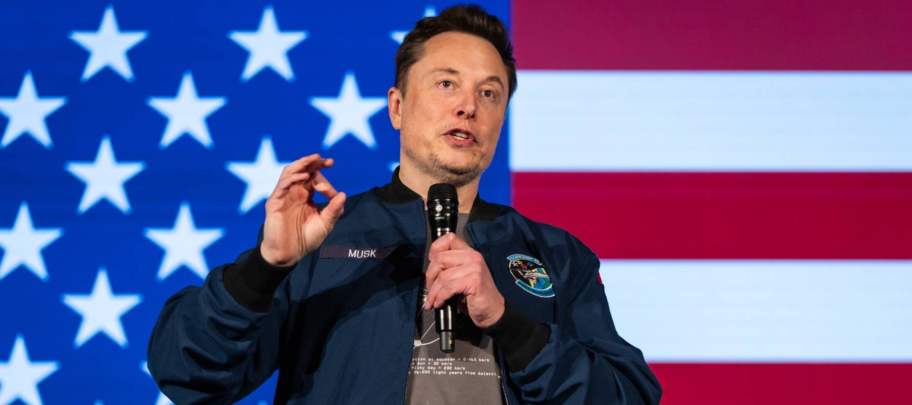 Elon musk speaks in front of the U.S. flag.