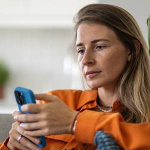 Middle-aged woman deeply focused on phone browsing.