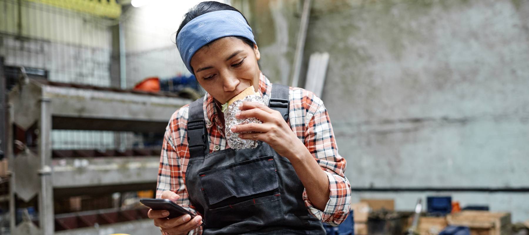 A young worker in overalls enjoys a sandwich during her lunch break.