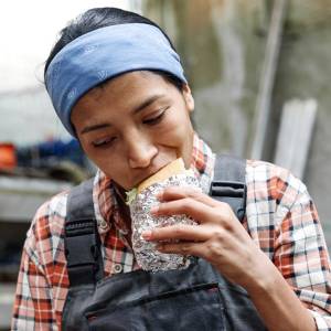 A young worker in overalls enjoys a sandwich during her lunch break.