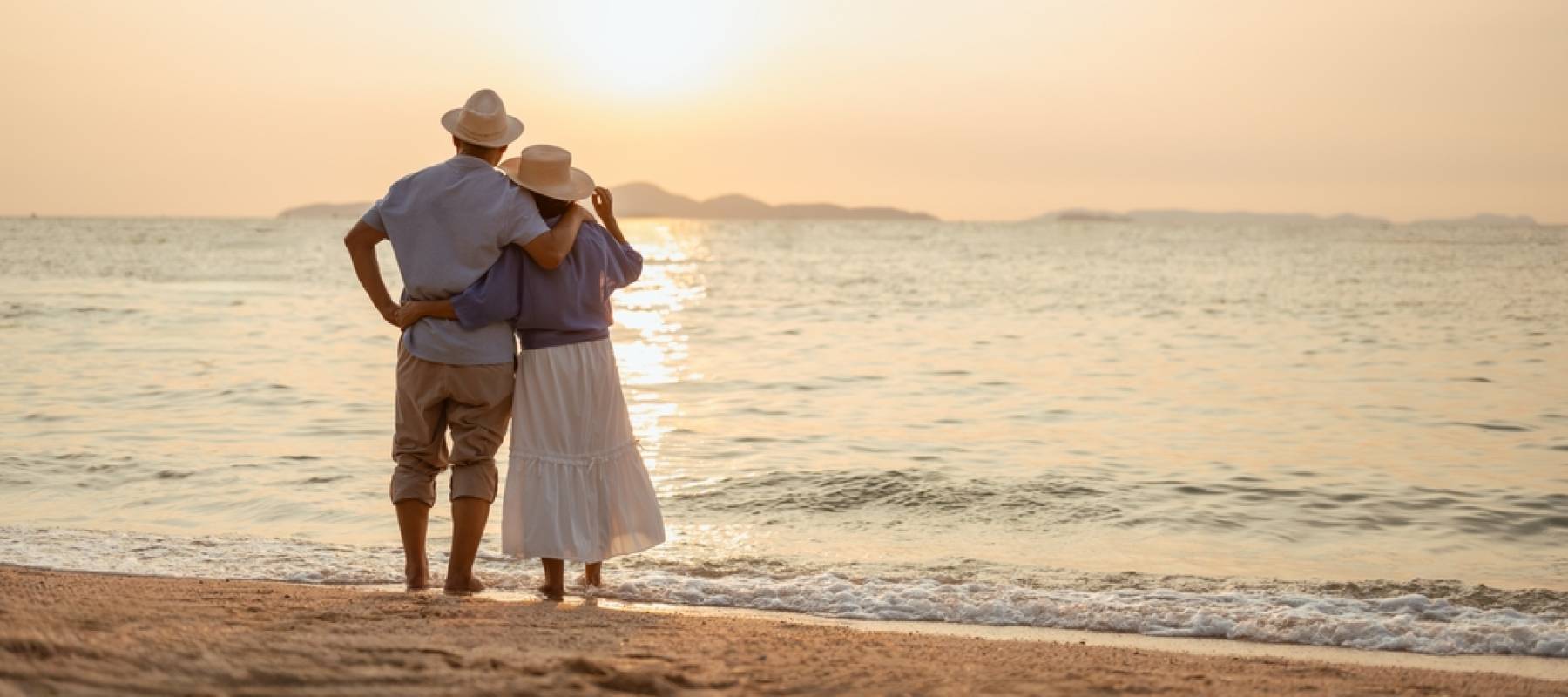 A retired couple standing on the beach at sunset.