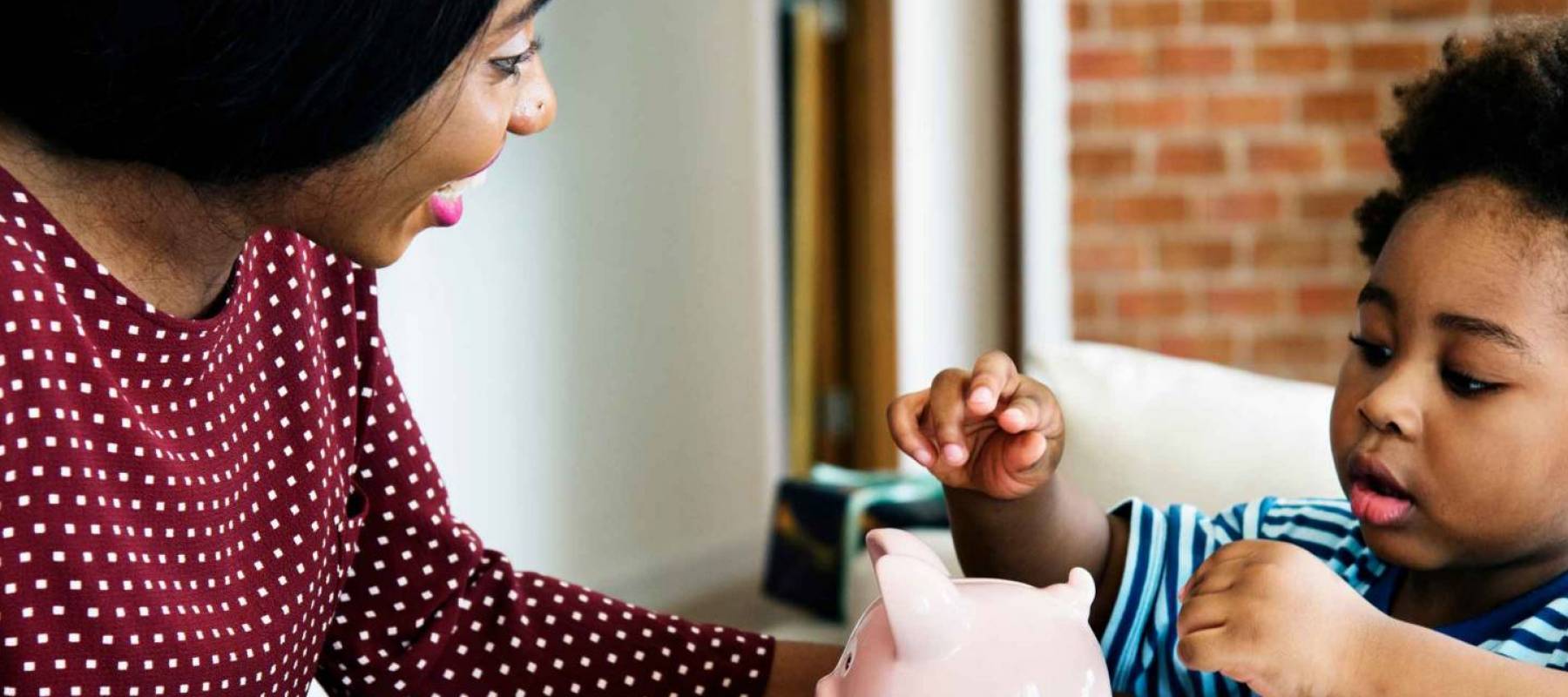 Adult with child putting money in piggy bank
