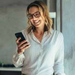 Smiling businesswoman using phone in office. Small business entrepreneur looking at her mobile phone and smiling.