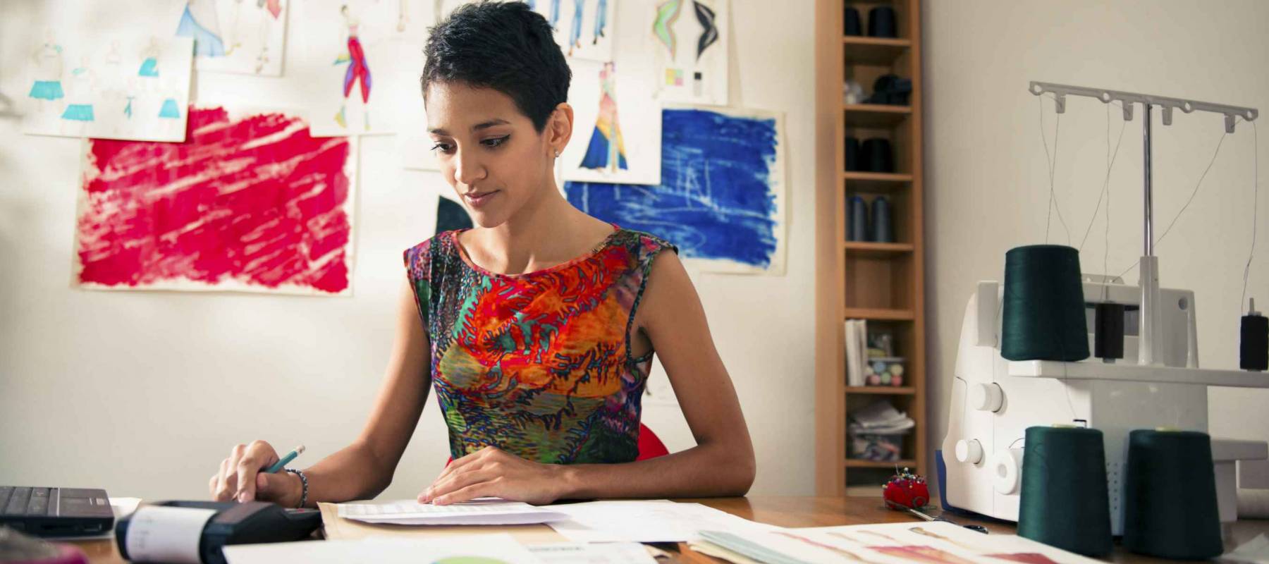 Money and financial planning, young hispanic self-employed woman checking bills and doing budget with calculator, computer and papers in fashion design studio