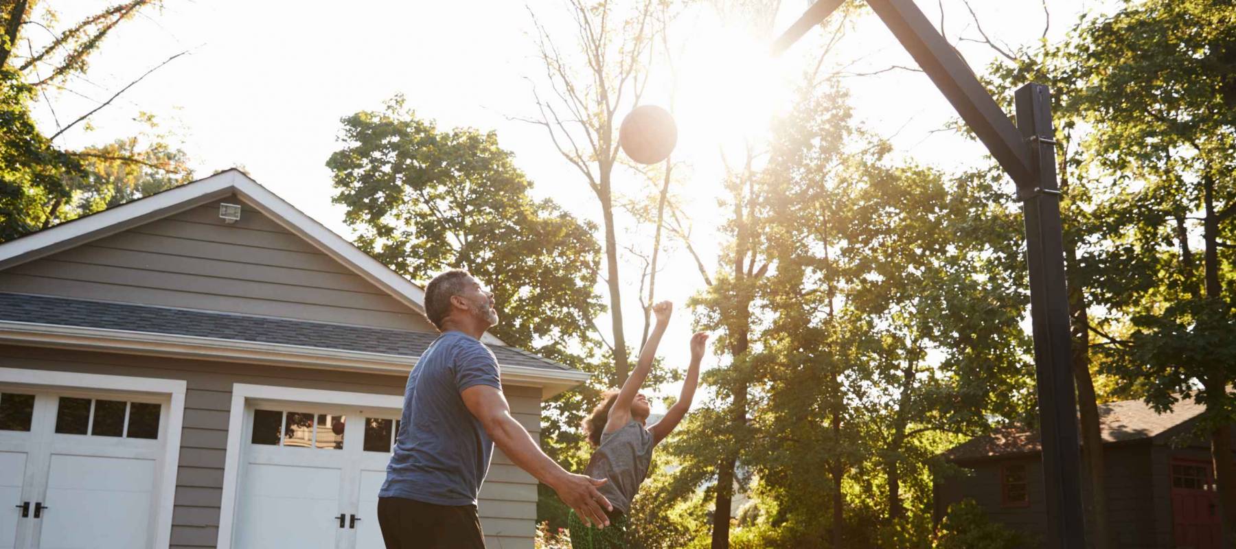 Father And Son Playing Basketball On Driveway At Home