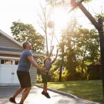 Father And Son Playing Basketball On Driveway At Home