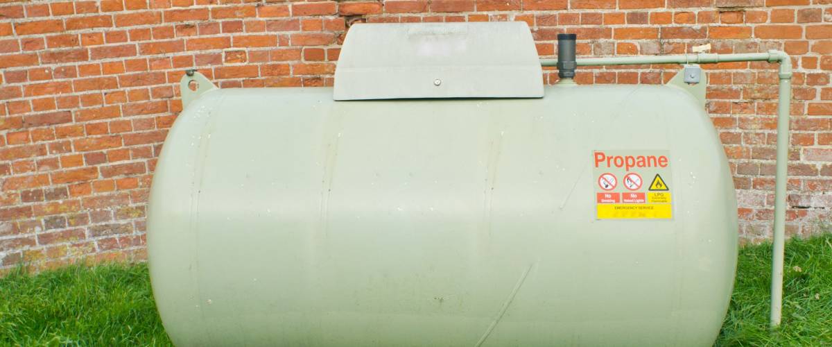 A large propane tank against a red brick wall