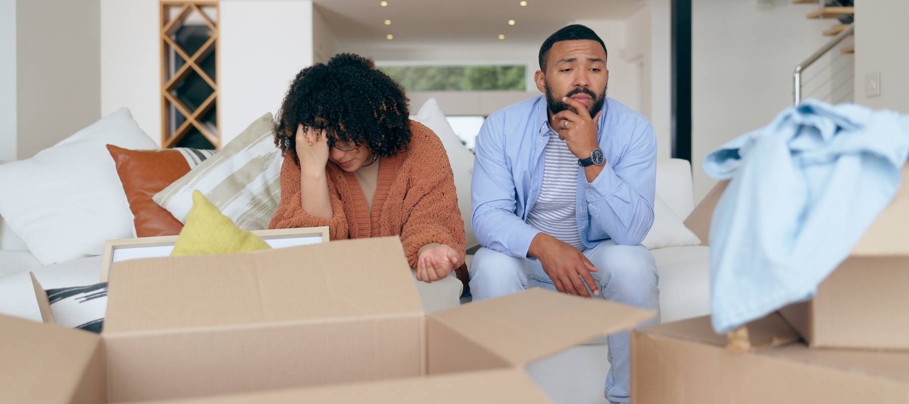 A couple surrounded by moving boxes, worried about housing costs.