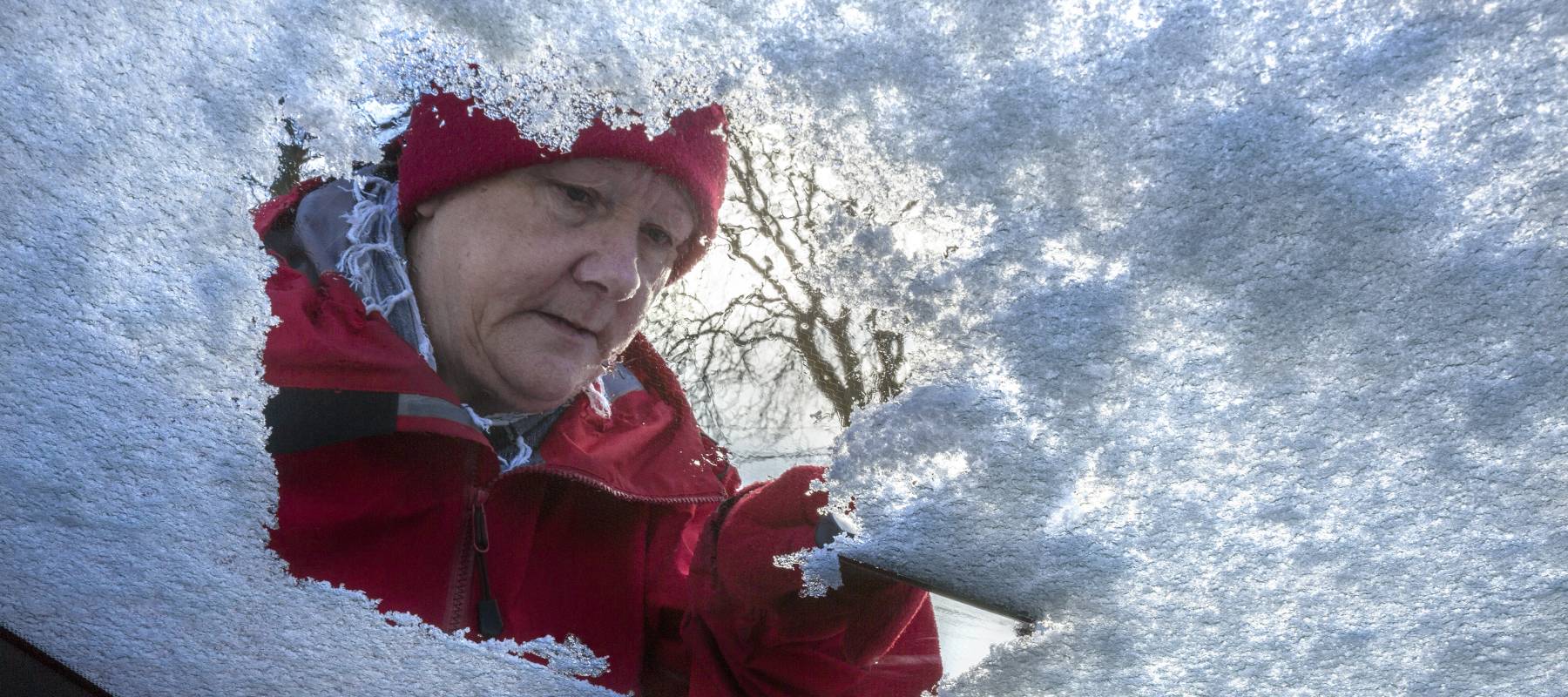 Older person clearing snow from their windshield.
