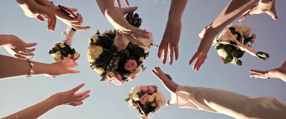 Women's hands trying catch four beautiful brides bouquets of roses pastel colors on clear blue sky background, horizontal photo