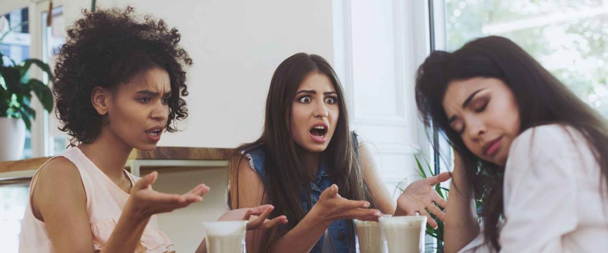 Young irritated girls at a loss from the actions of a friend, arguing in cafe and drinking coffee, panorama, copy space