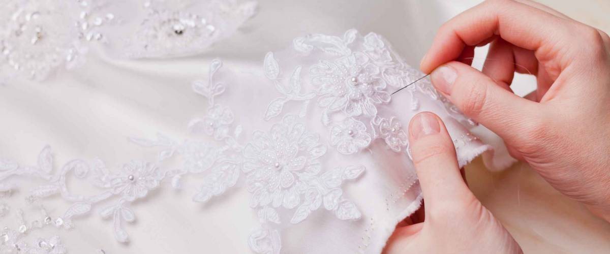 woman hands close up sewing a wedding dress, white material decorated with lace, tailoring clothes, white fabric