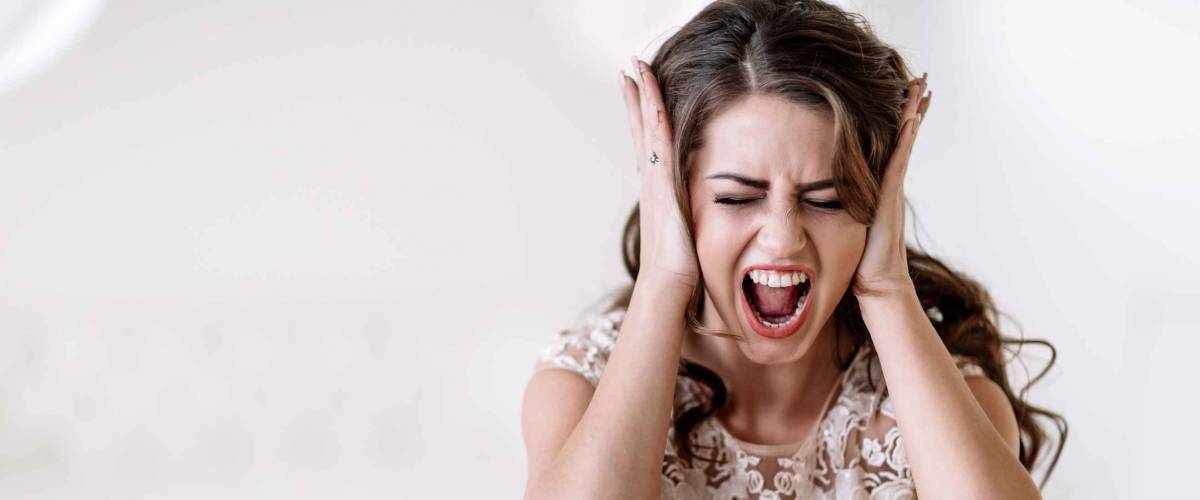 portrait of the bride shouts loudly covering his ears with his hands, furious. Natural light. Eyes closed
