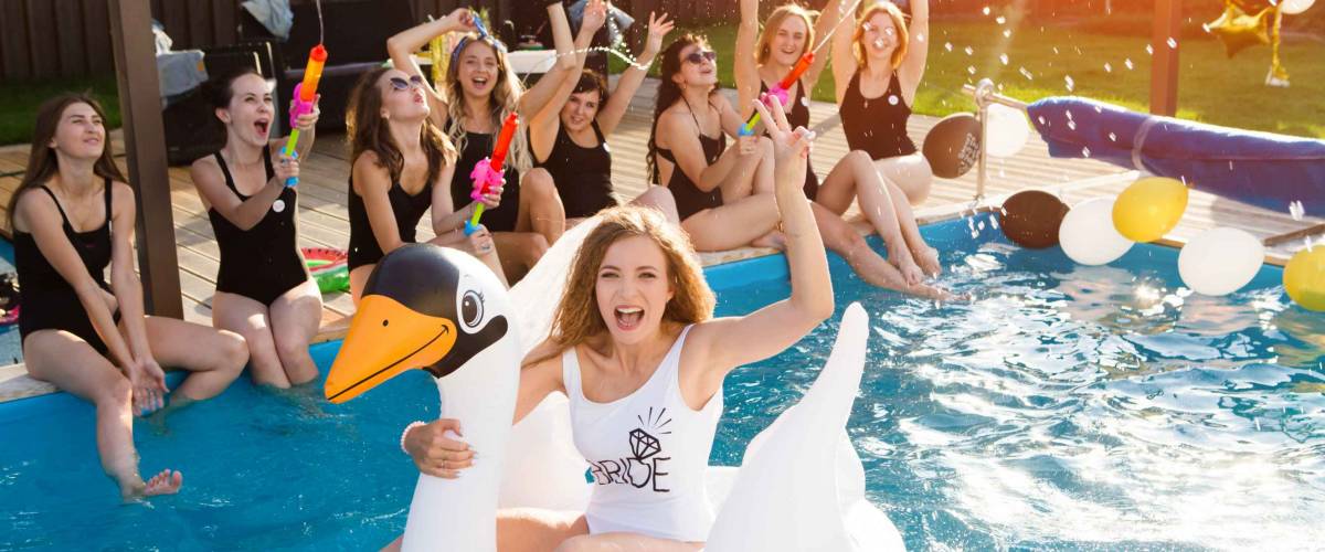 happy  beautiful girlfriends having a great time at the hen party. Attractive young women bride floating on a big inflatable swan in pool.