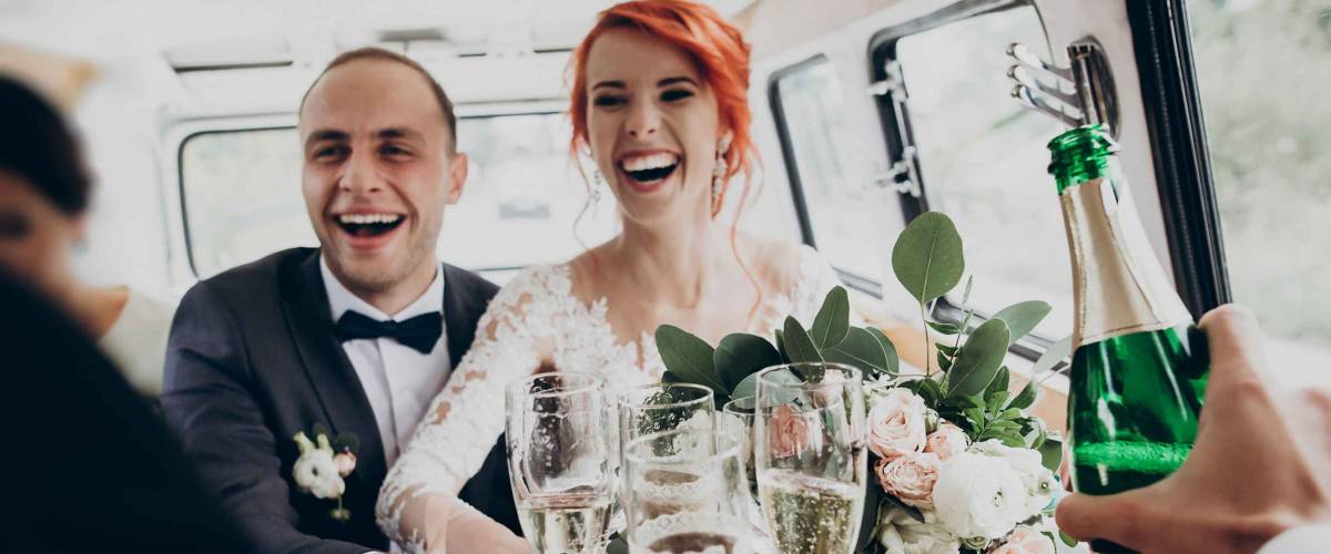 stylish happy bride and groom toasting with glasses of champagne and having fun with bridesmaids and groomsmen inside of retro car. emotional moment, space for text. wedding party