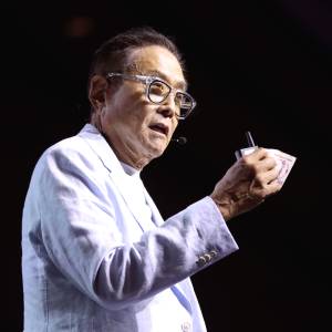 Robert Kiyosaki holds up some bills while wearing a pure white suit