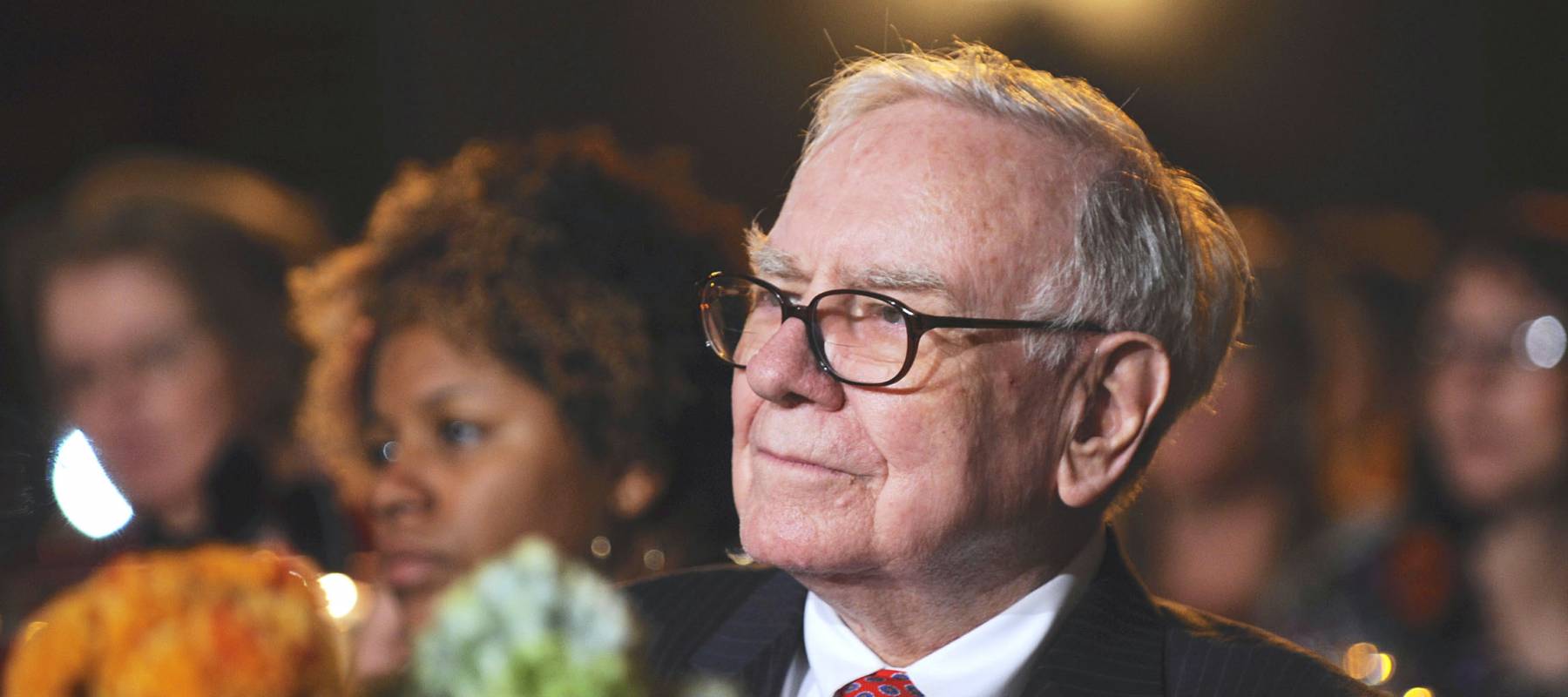 Warren Buffett sits at a table, listening at an event