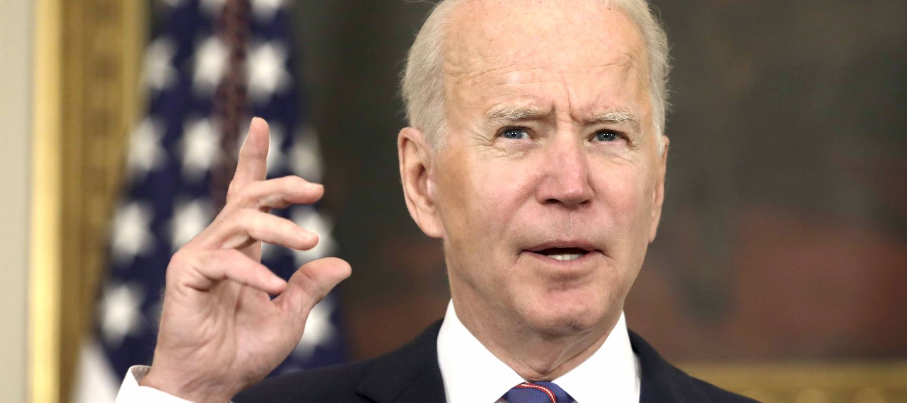 President Joe Biden speaks at a podium with one hand up, making a gesture