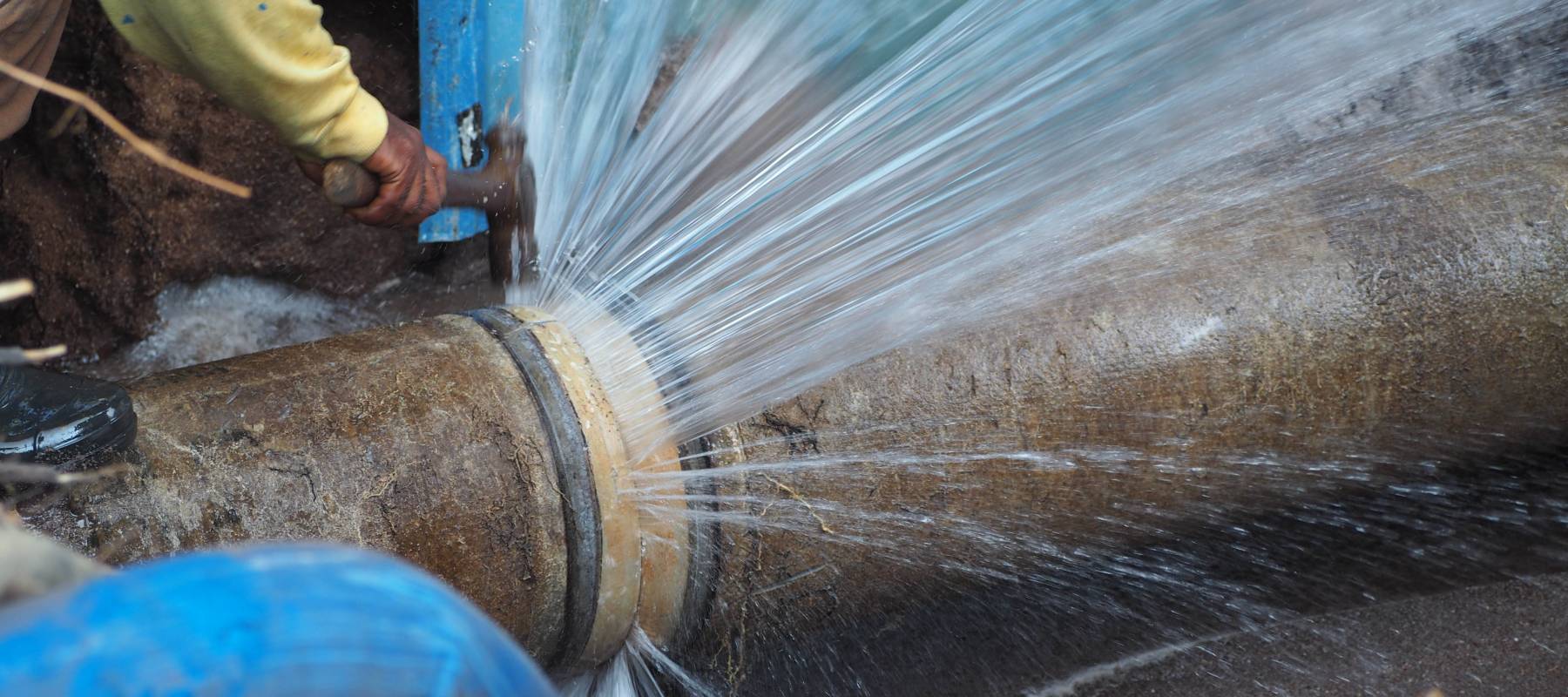 Water shooting out of a burst pipe in a hole.