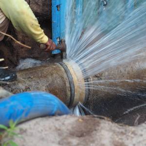 Water shooting out of a burst pipe in a hole.