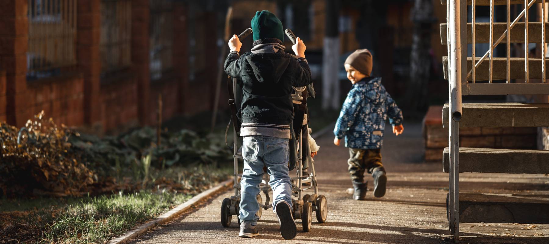 Two children walking down an alleyway, one with a stroller.