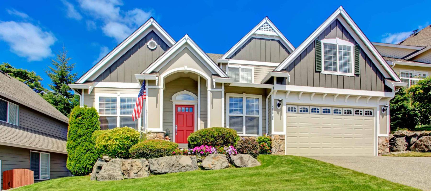 Grey house exterior with entrance porch and red door. Beautiful front yard landscape with vivid flower and stones