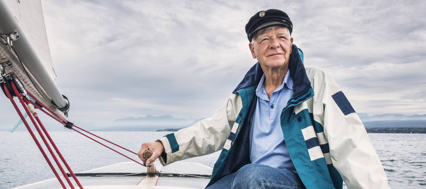 An older man steers a sailboat, one hand on the rudder and eyes on the horizon.