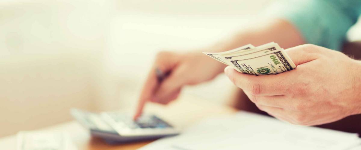 close up of man with calculator counting money and making notes at home