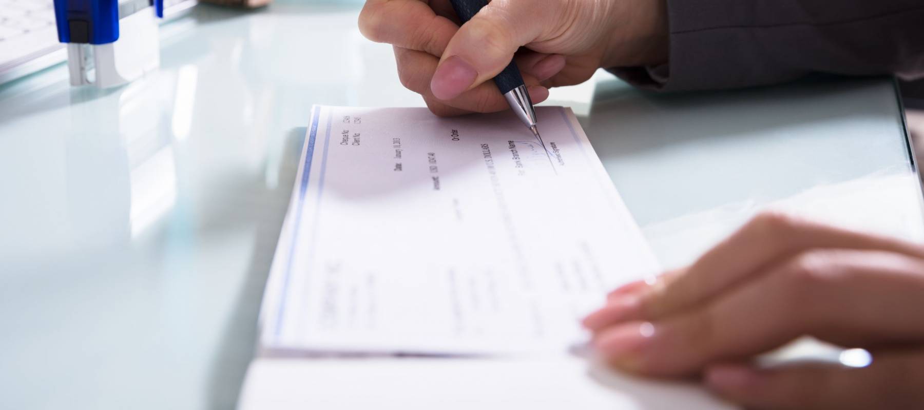 Close-up Of A Businessperson&#039;s Hand Signing Cheque With Pen In Office