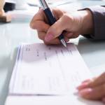 Close-up Of A Businessperson's Hand Signing Cheque With Pen In Office