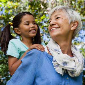 Low angle view of happy grandmother giving piggyback to granddaughter against trees.