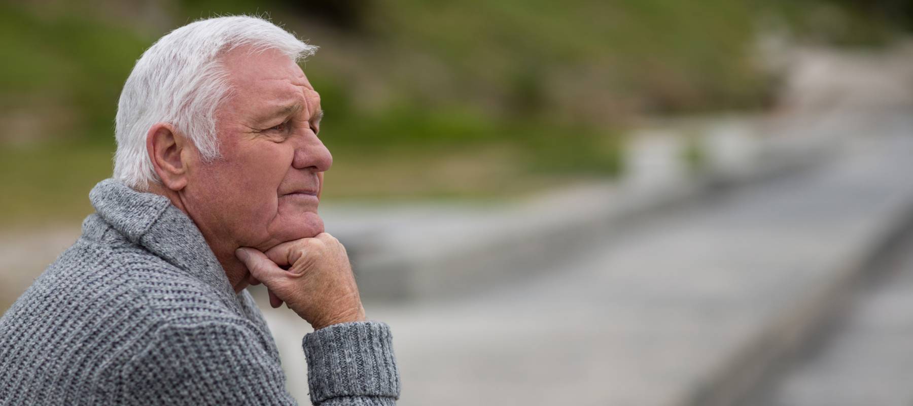 White-haired man sitting on the steps near beach in a contemplative pose.